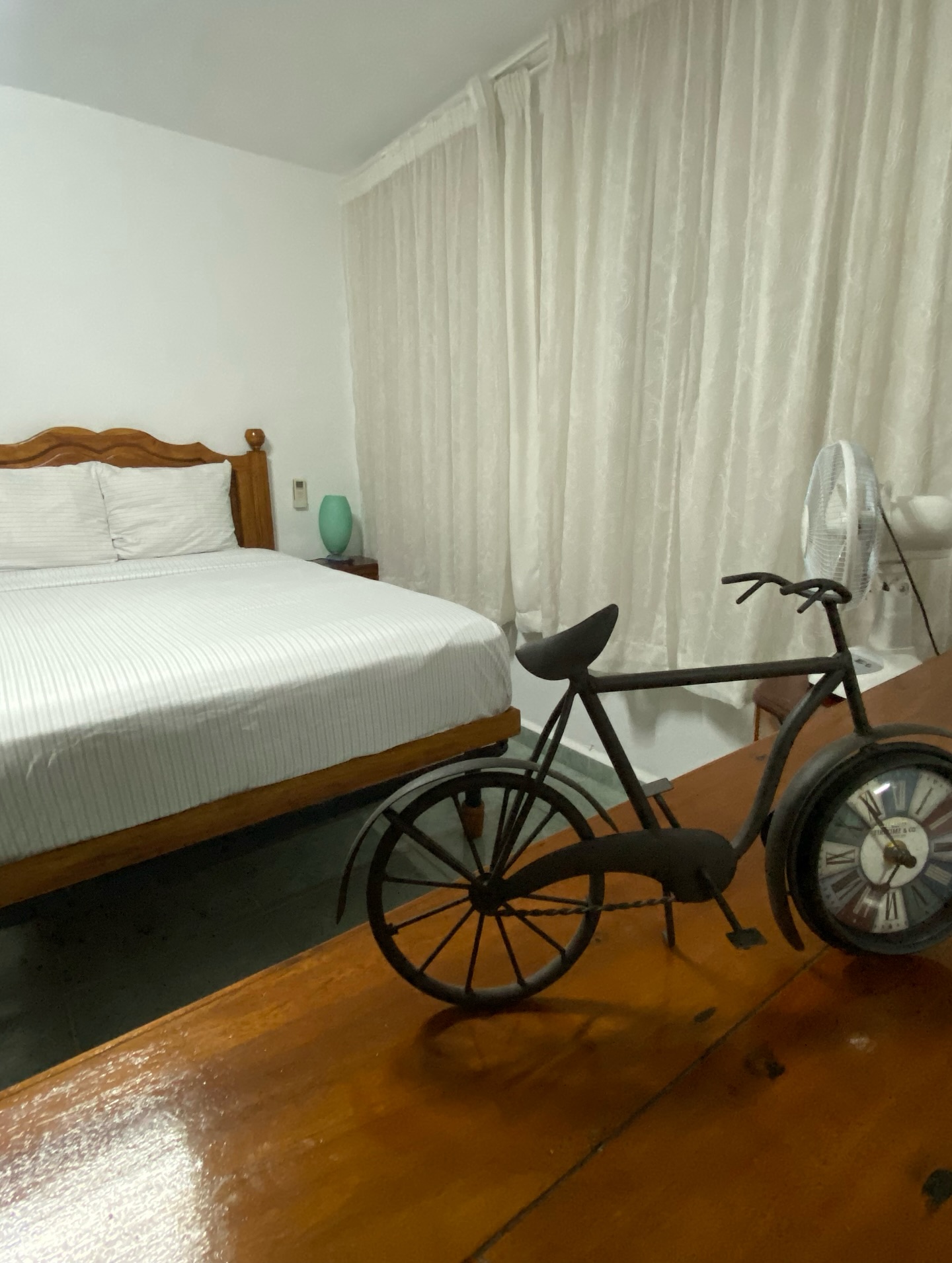 Bright double room with white bedding, wooden floor and a paseo bicycle in the foreground