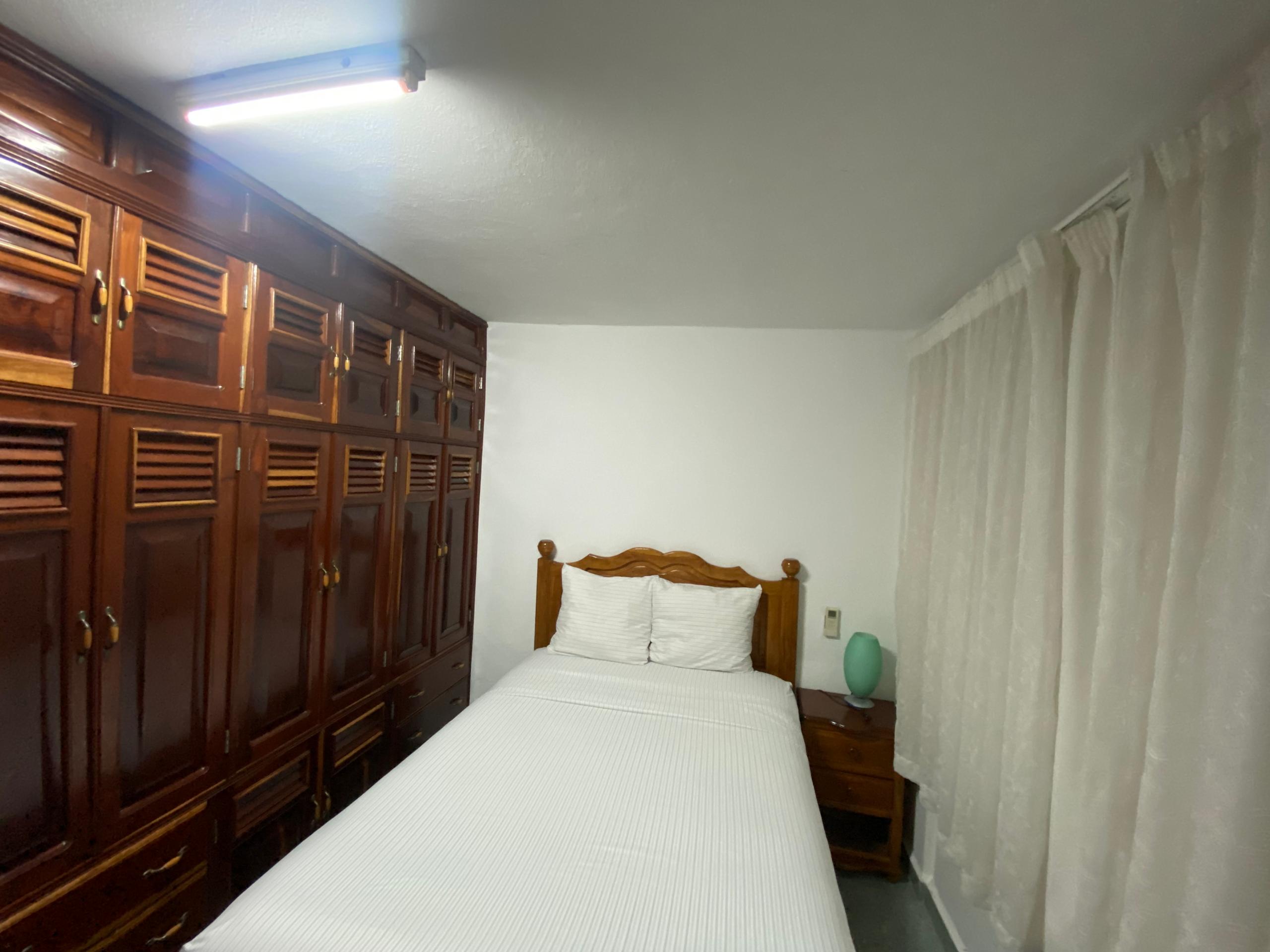 Single-bed room with a wall of mahogany louvred wardrobes and white linens