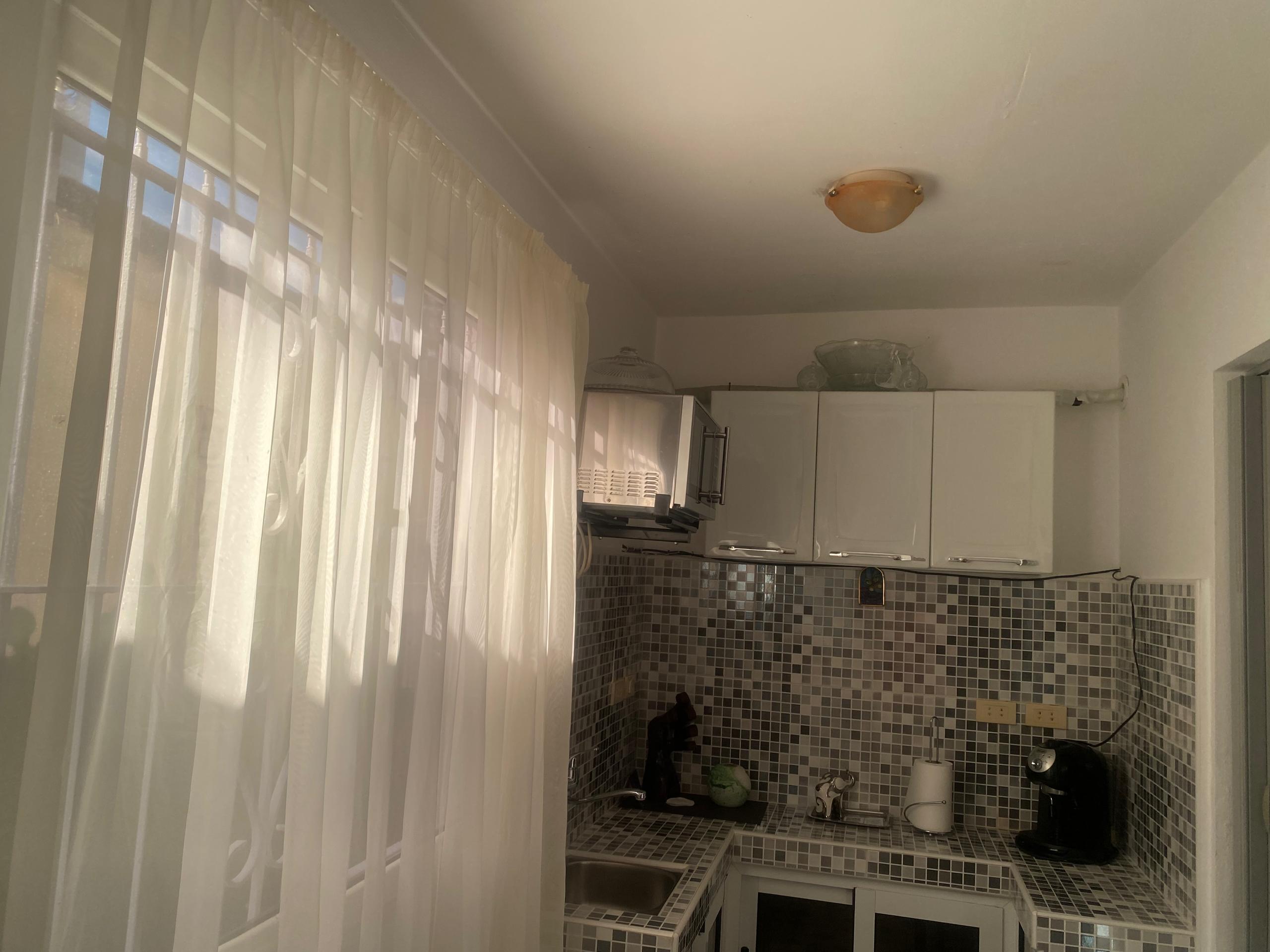 Modern white kitchen with mosaic-tiled backsplash, coffee machine and sheer curtains