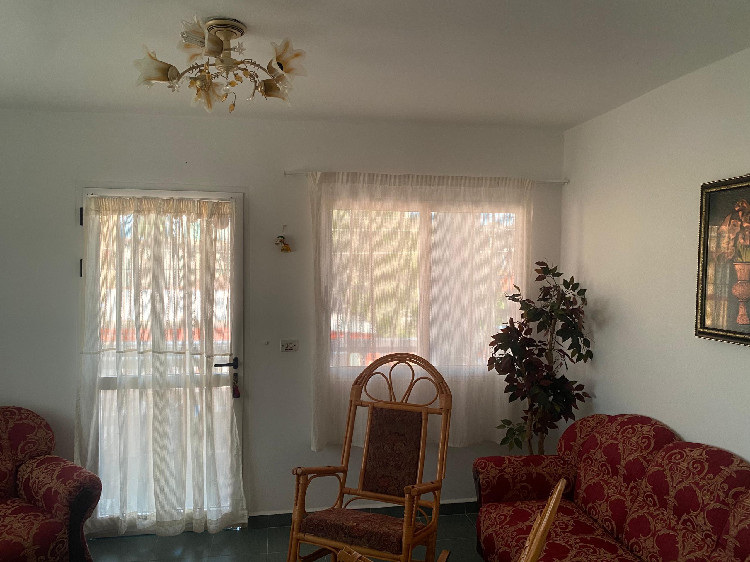 Communal sitting room with crimson sofas, wicker rocker, sheer curtains and a chandelier