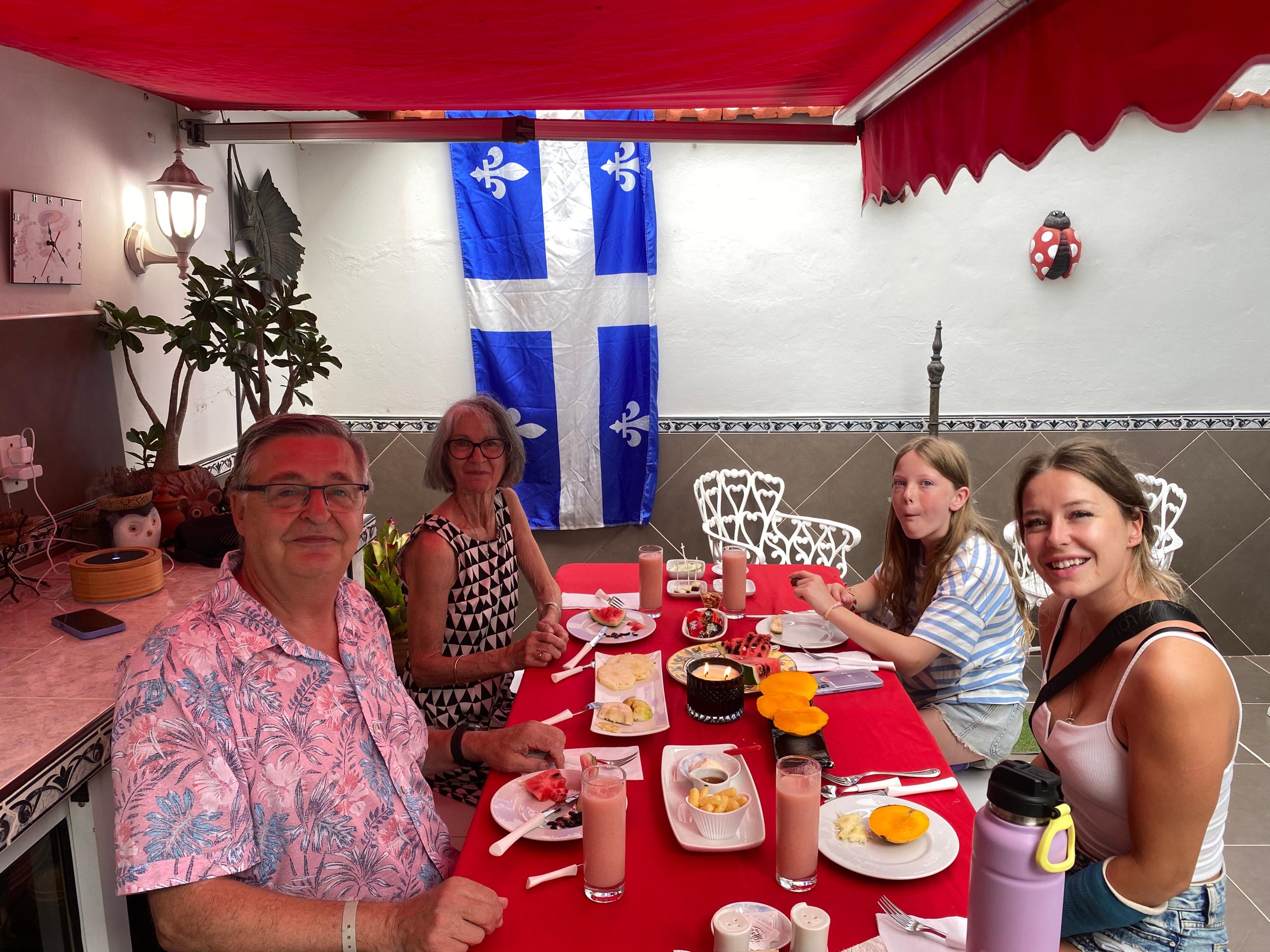 A family of guests around the breakfast table on the terrace at Hostal Jose Cuba, the Quebec flag in the background
