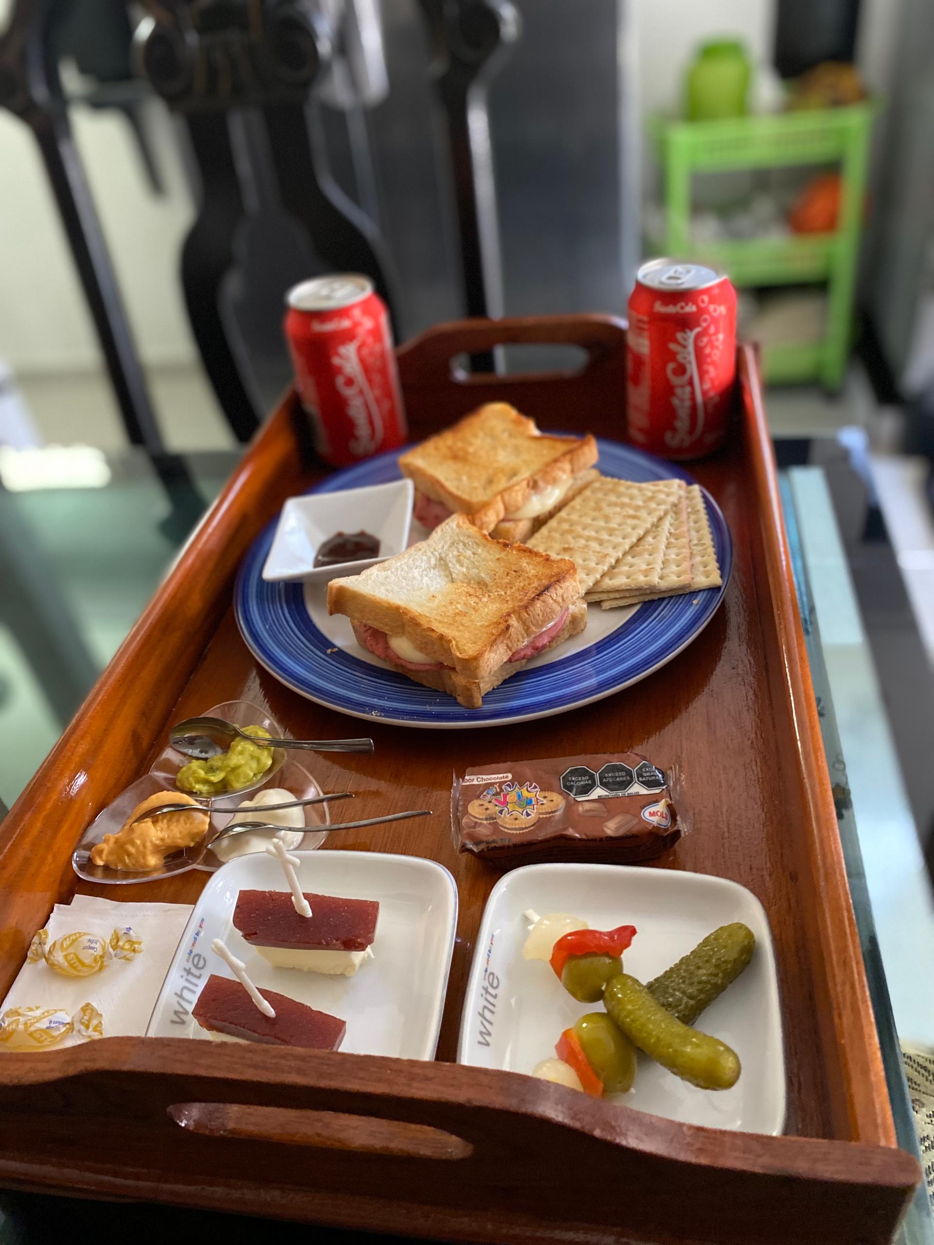 Breakfast tray with toasted sandwiches, drinks, jam, cheese and pickles by candlelight
